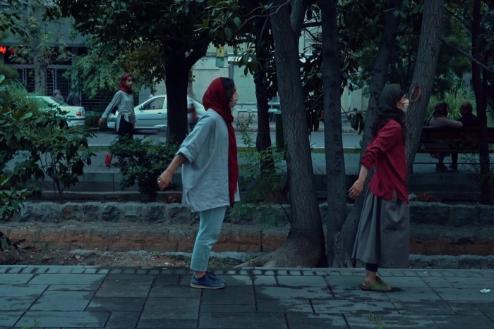 A still from a film, depicting two women in hijab on a street, their hands outstretched backwards in a dance gesture